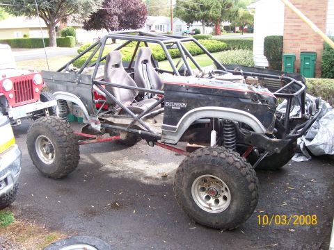 1984 Ford Bronco - A heavily modified vehicle with a roll cage and racing seats is shown in a driveway, with another vehicle partially visible.