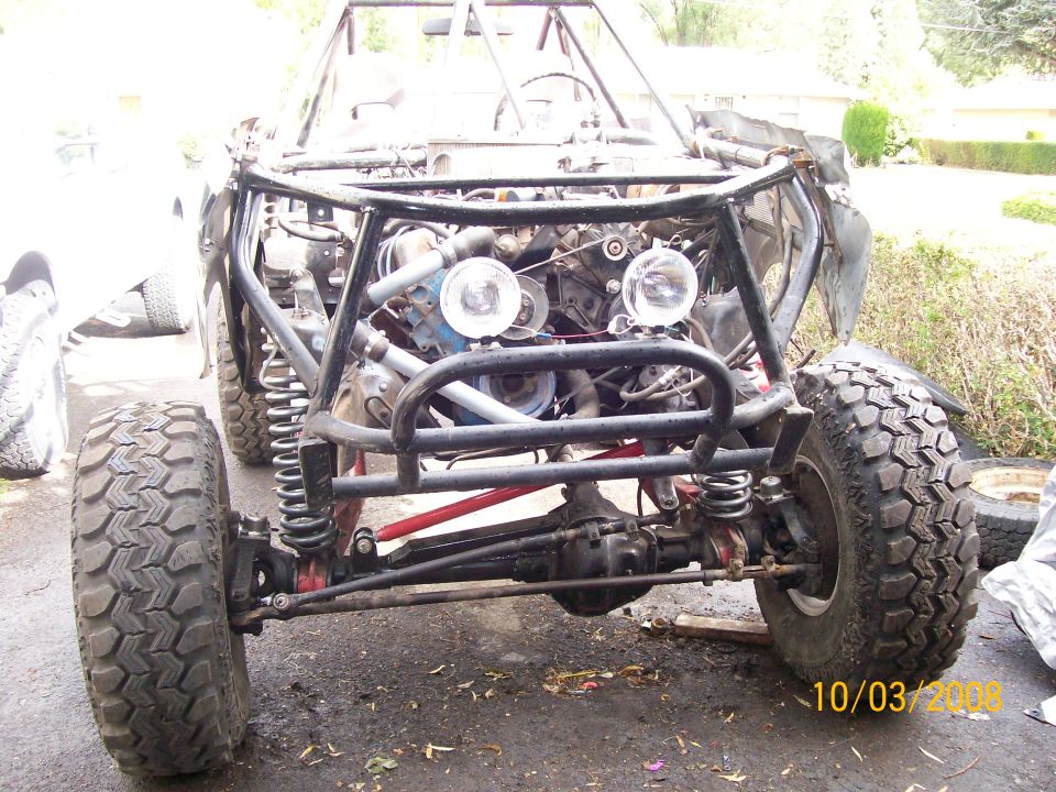 Off-road buggy chassis with exposed engine, front suspension, and large tires. Roll cage visible