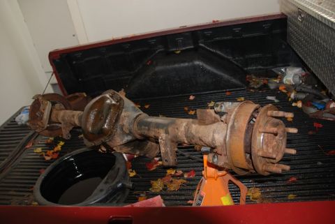 1996 Ford Bronco - A used rear axle assembly sits in the bed of a red pickup truck, surrounded by fallen leaves.