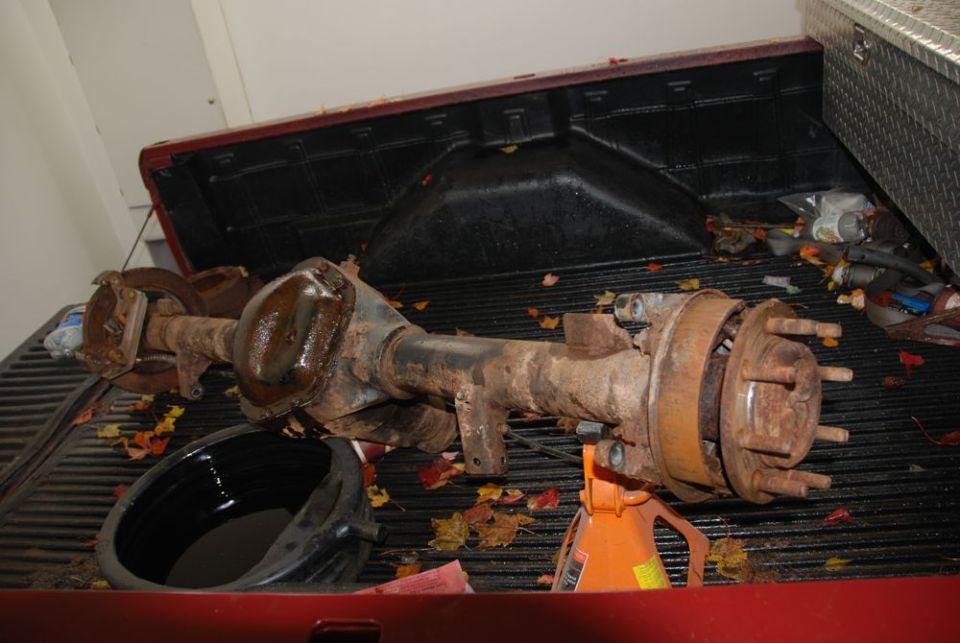 Rusty rear axle assembly with brake drums, resting on an orange jack stand in a truck bed
