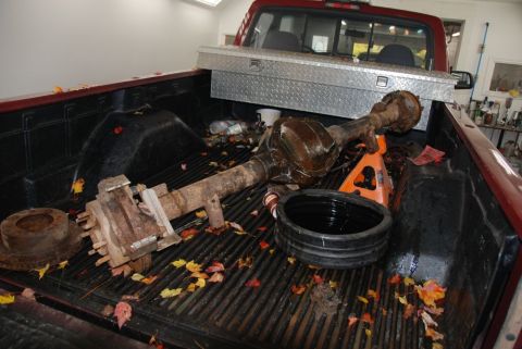 1996 Ford Bronco - A rusty rear axle assembly is loaded into the bed of a red pickup truck, along with a toolbox and other items.