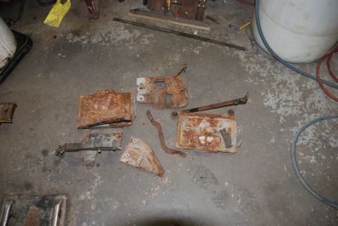 1996 Ford Bronco - Rusted metal parts, possibly from a vehicle, lie on a garage floor.