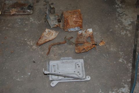 1996 Ford Bronco - Several heavily corroded metal components, possibly from a vehicle's engine bay, are scattered on a workshop floor.