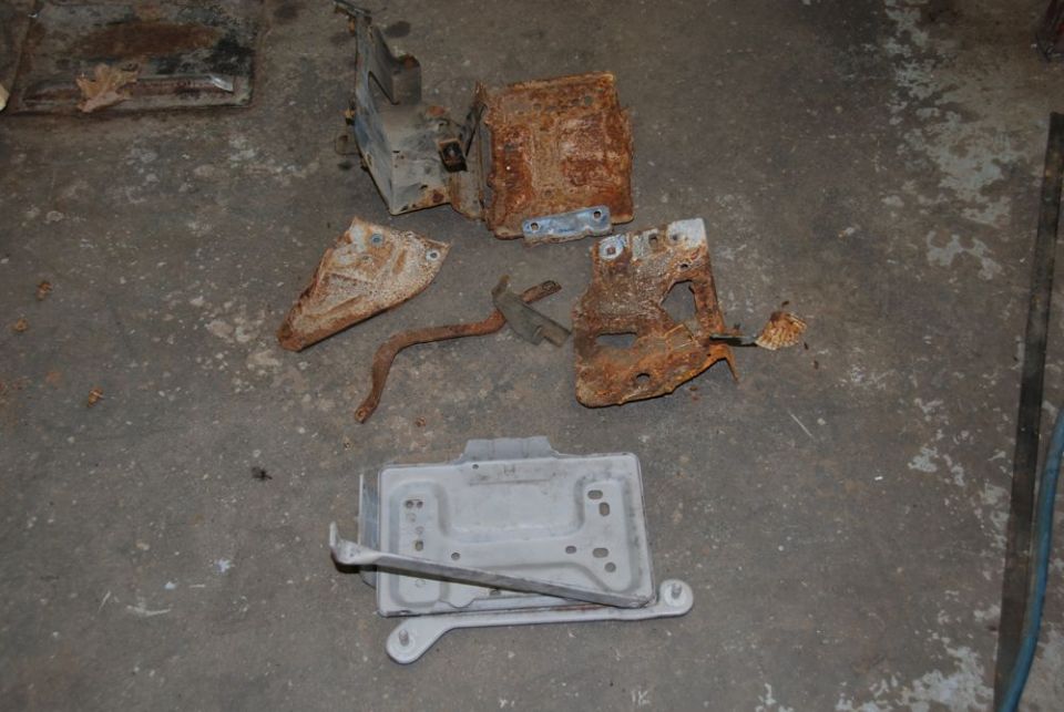 Pile of heavily rusted metal brackets and a battery tray on a concrete floor