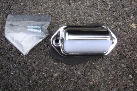 1996 Ford Bronco - A new chrome license plate light assembly and its mounting hardware are shown on a dark, textured surface.