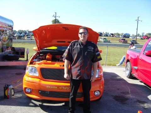 2007 Ford Mustang - Man poses with his modified orange 2004 Ford F-150 pickup truck at an outdoor event.