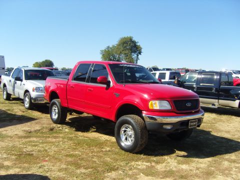 2007 Ford Mustang - A red Ford F-150 truck is parked in a lot with other vehicles under a clear blue sky.