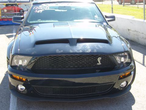 2007 Ford Mustang - A black Ford Mustang Shelby GT500 is seen from the front, with '2008 SST' written on the windshield. Another classic car is visible in the…