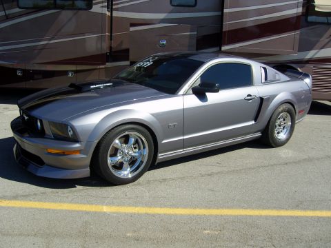 2007 Ford Mustang - A silver 2007 Ford Mustang GT is parked in front of a large RV, black racing stripes and chrome wheels.