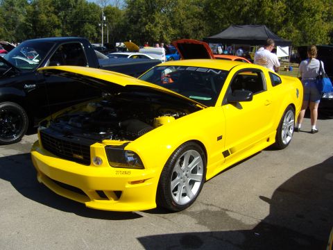 2007 Ford Mustang - A bright yellow Saleen Mustang is displayed with its hood up at an outdoor event, surrounded by other vehicles and tents.