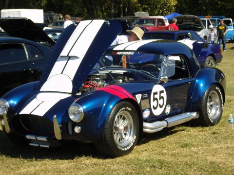 2007 Ford Mustang - A blue Shelby Cobra replica is displayed at an outdoor car show with other vehicles in the background.