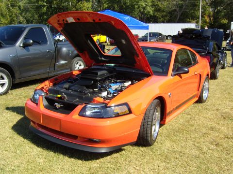 2007 Ford Mustang - Orange Ford Mustang parked on grass with hood open, next to a gray pickup truck.