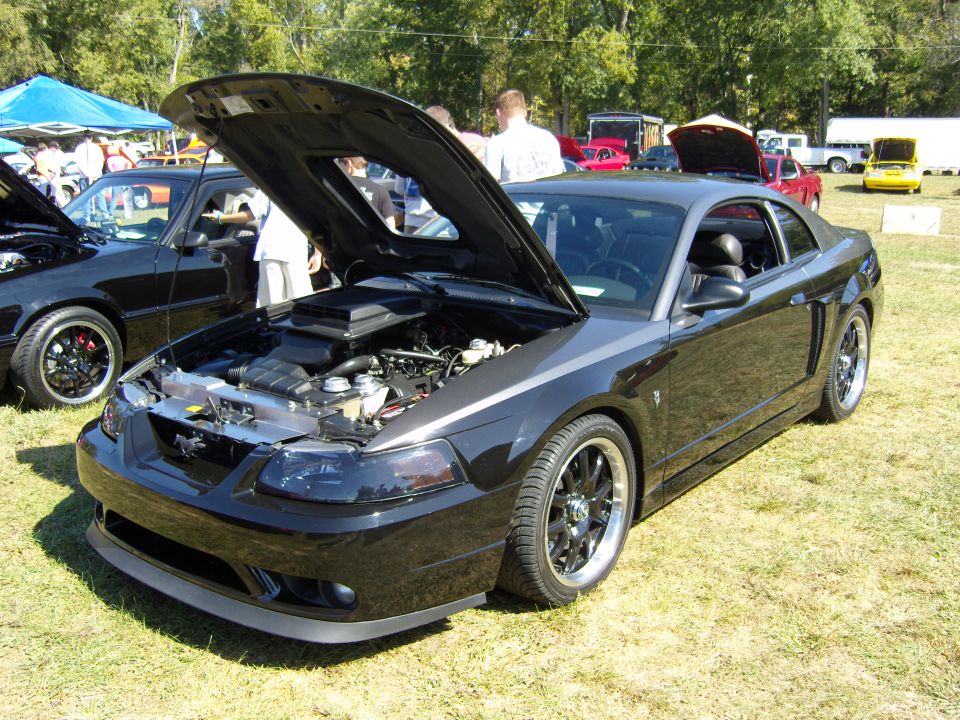 Black Ford Mustang with hood open, showing engine. Dark tinted headlights, aftermarket wheels