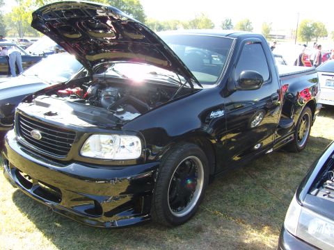 2007 Ford Mustang - A black Ford F-150 Lightning pickup truck is displayed with its hood open, revealing the engine bay and custom wheels.