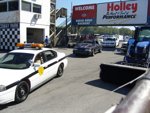 2007 Ford Mustang - A dark Ford Mustang is parked at Beech Bend Raceway, with a police car and a tractor nearby.