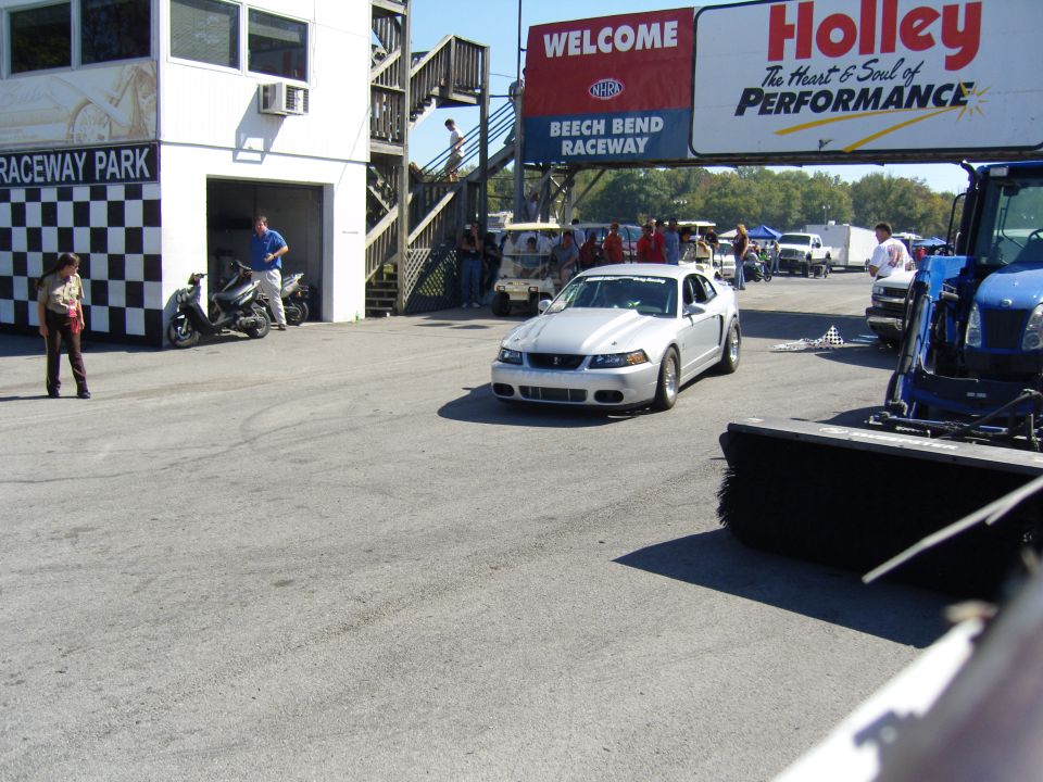Silver coupe with racing stripes on the hood, seen from a 3/4 front angle at a racetrack