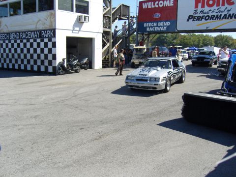 2007 Ford Mustang - Silver Mustang on track at Beech Bend Raceway, with other vehicles and structures in the background.