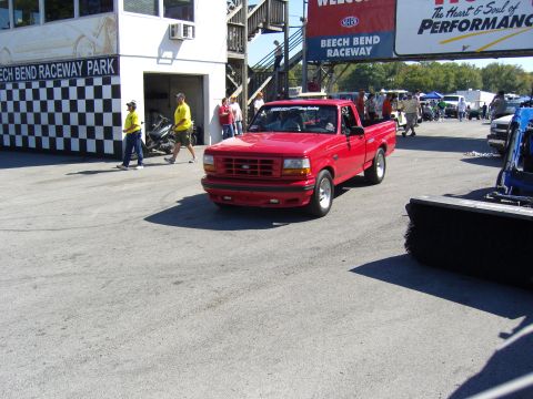 2007 Ford Mustang - A red pickup truck drives past the Beech Bend Raceway Park building.