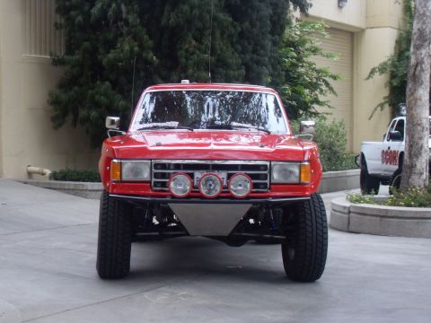 1990 Ford Bronco - A red off-road truck is parked outside, with another white vehicle visible in the background.