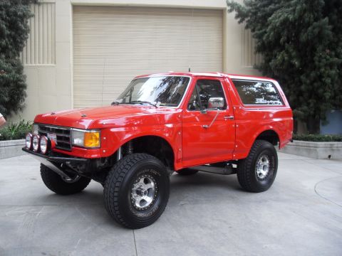 1990 Ford Bronco - This lifted red Ford Bronco sits parked in front of a garage door.