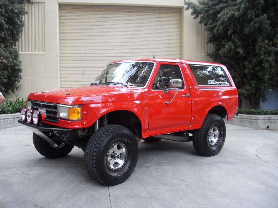Red Ford Bronco with aftermarket bumper and lights, lifted suspension, and off-road tires