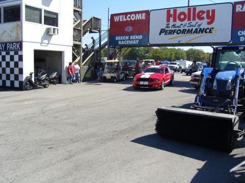 2007 Ford Mustang - A red Ford Mustang with white racing stripes is seen at Beech Bend Raceway, with a blue tractor in the foreground.