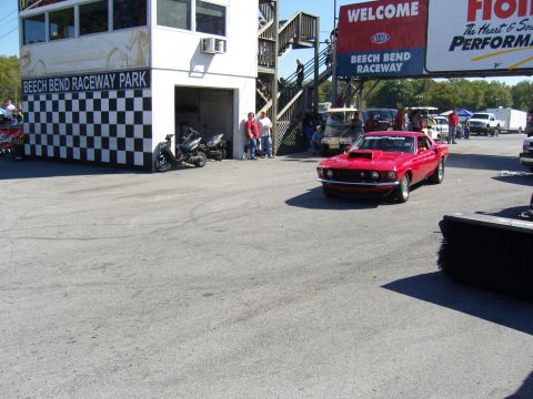 2007 Ford Mustang - A red classic car drives past the Beech Bend Raceway Park building.