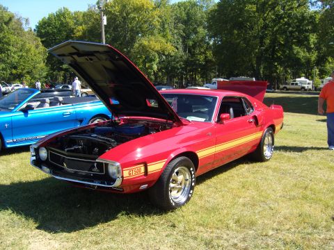 2007 Ford Mustang - A classic red 1969 Ford Mustang GT500 is displayed with its hood open, parked next to a blue convertible.