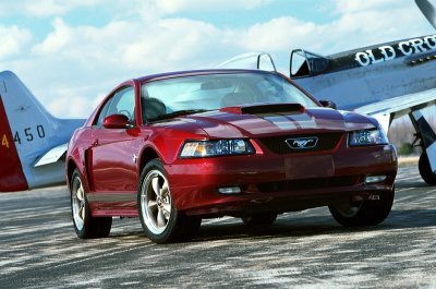 2004 Ford Mustang - A red 2004 Ford Mustang is parked on an asphalt surface next to a vintage airplane.
