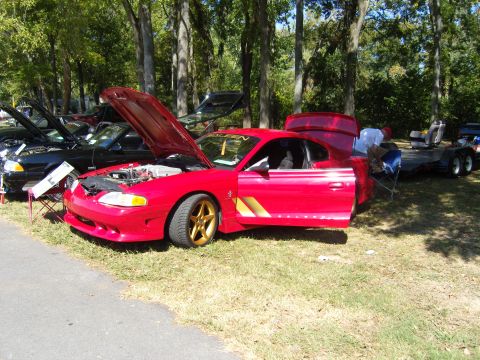 2007 Ford Mustang - A red coupe with gold accents and gold wheels is displayed with its hood and door open, alongside other vehicles.