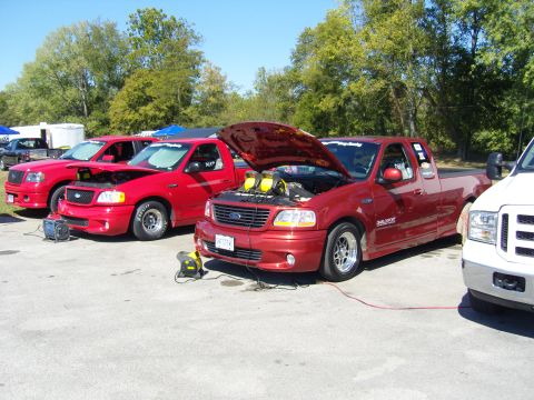 2007 Ford Mustang - Several red Ford F-150 SVT Lightning trucks are parked outdoors, with two showing their engines under open hoods.