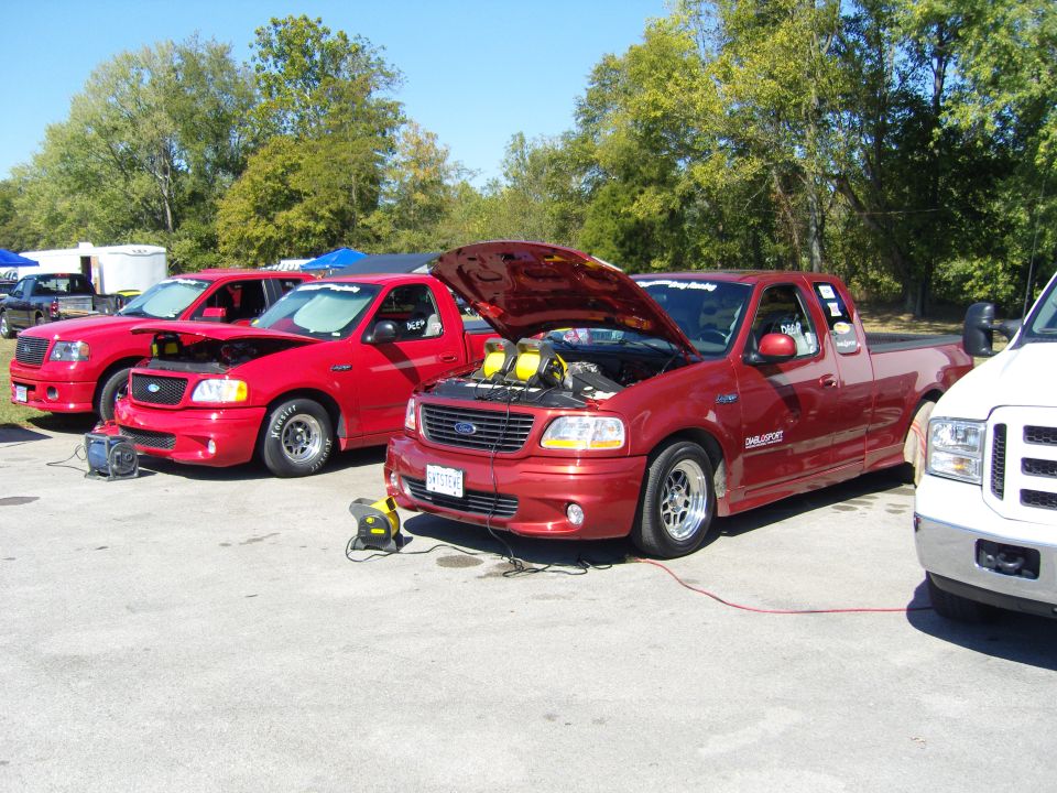 Three red Ford F-150 SVT Lightning pickup trucks lined up, two with hoods open. A white Ford truck is partially visible on the right