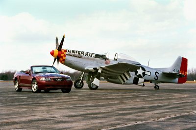 2004 Ford Mustang - A red 2004 Ford Mustang convertible sits on the tarmac beside a P-51 Mustang aircraft.