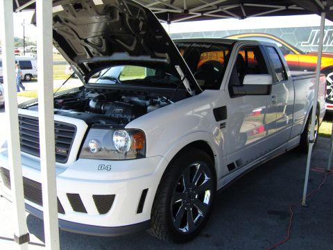 2007 Ford Mustang - A white pickup truck is parked with its hood open, revealing the engine compartment. The vehicle has custom wheels and a "04" badge on the…