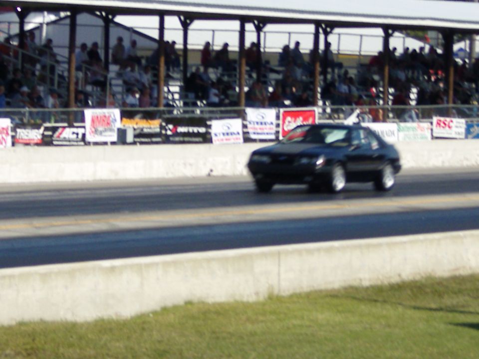 Black coupe on a racetrack, spectators in background