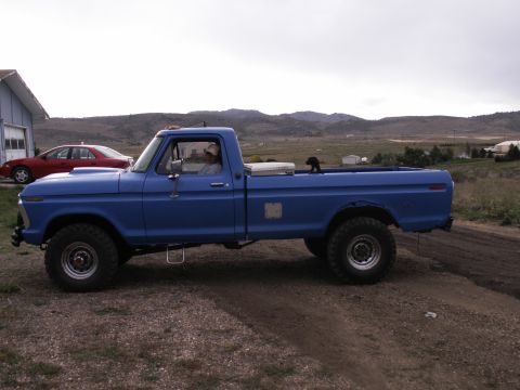 1977 Ford F-250 - A blue 1977 Ford F-250 pickup truck is parked on a dirt road in front of a building and a red sedan. The truck has a toolbox mounted in the…