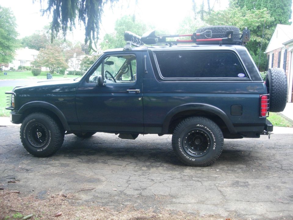 Dark blue 1993 Ford Bronco with off-road tires and roof rack, side view.