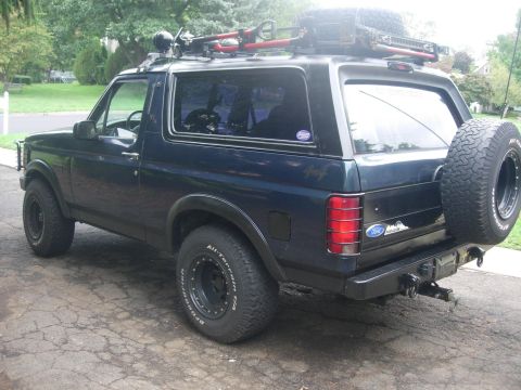 1993 Ford Bronco - The rear of a black 1993 Ford Bronco is visible, equipped with a roof rack and a spare tire.