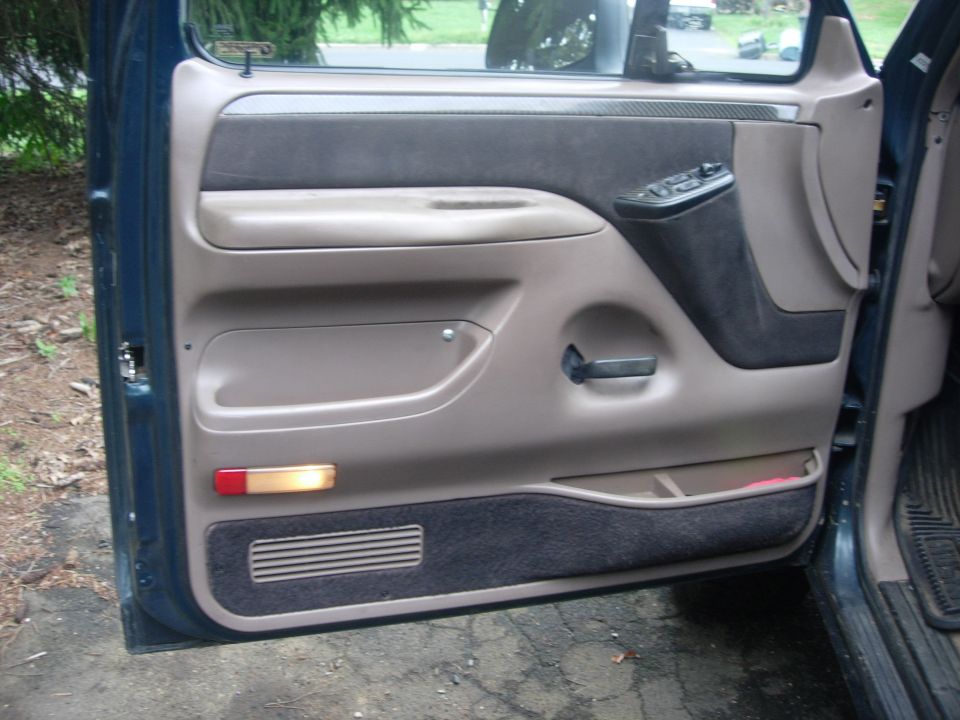 Interior driver's side door panel of a dark blue Ford Bronco. Tan and dark gray fabric, chrome handle, power controls.