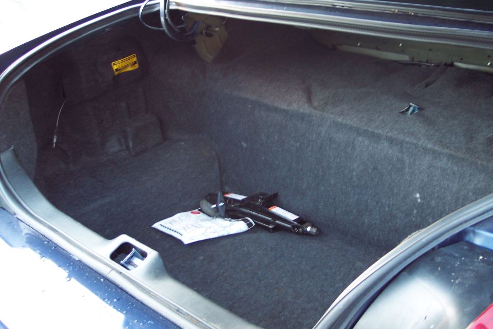 Open trunk of a dark blue sedan with a jack and manual inside.