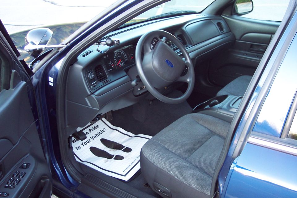 Interior of a blue Ford Crown Victoria, showing dashboard, steering wheel, seat, and floor mat.