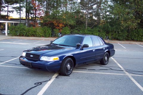 2001 Ford Crown Victoria - A dark blue 2001 Ford Crown Victoria sedan is parked in an outdoor lot with trees in the background.