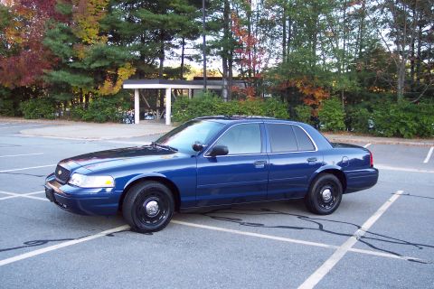 2001 Ford Crown Victoria - A blue sedan is parked in a lot with trees in the background.
