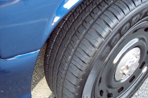 2001 Ford Crown Victoria - Close-up of a blue vehicle's fender and tire, showing a black steel wheel and hubcap.