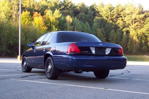 2001 Ford Crown Victoria - Rear view of a dark blue 2003 Ford Crown Victoria sedan parked in an asphalt lot with trees in the background.