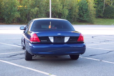 2001 Ford Crown Victoria - The rear of a blue 2001 Ford Crown Victoria is visible in a parking lot.