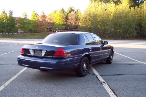 2001 Ford Crown Victoria - A blue Ford Crown Victoria is parked in an empty lot with trees in the background.