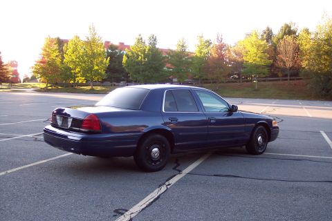 2001 Ford Crown Victoria - A dark blue 2001 Ford Crown Victoria sedan is parked in an empty lot on a sunny day.