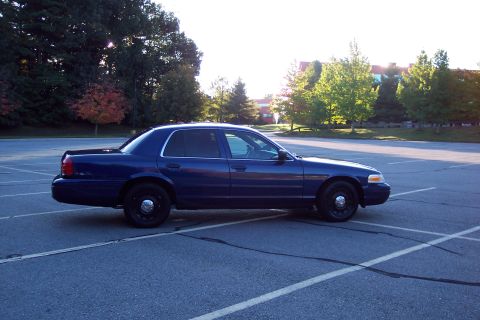 2001 Ford Crown Victoria - A dark blue 2001 Ford Crown Victoria is seen from the side in a parking lot with trees and buildings in the background.