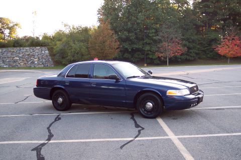 2001 Ford Crown Victoria - Dark blue 2001 Ford Crown Victoria parked in a lot with trees in the background.
